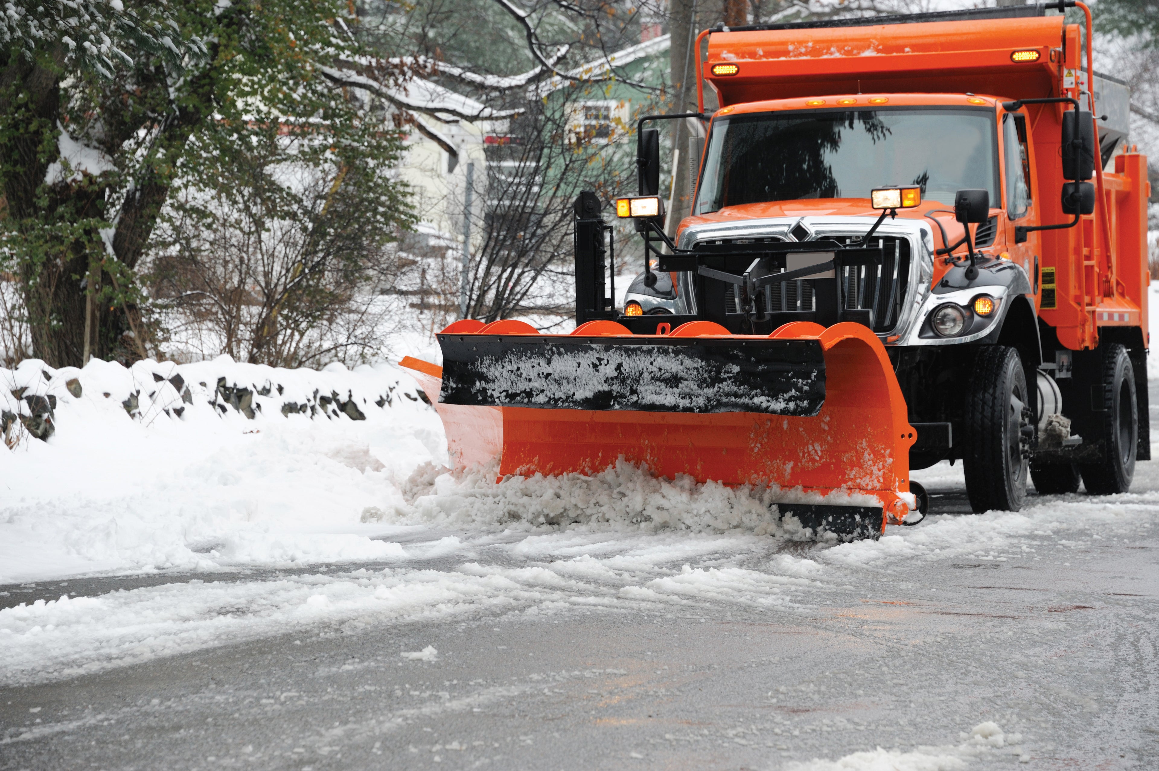 Orange snowplow plowing snow off of a residential street.